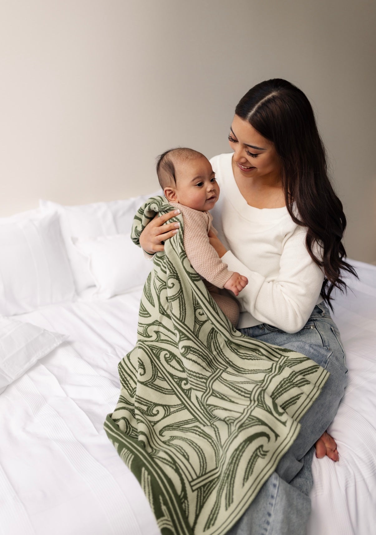 Woman holding a baby wrapped in a green patterned blanket on a bed.